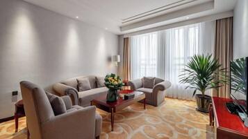 A hotel room with a sofa set, a coffee table, a TV, and a large window with curtains.