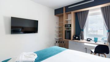 Una moderna camera d'albergo con un letto, una TV a parete, una scrivania con un computer e una finestra con tende.