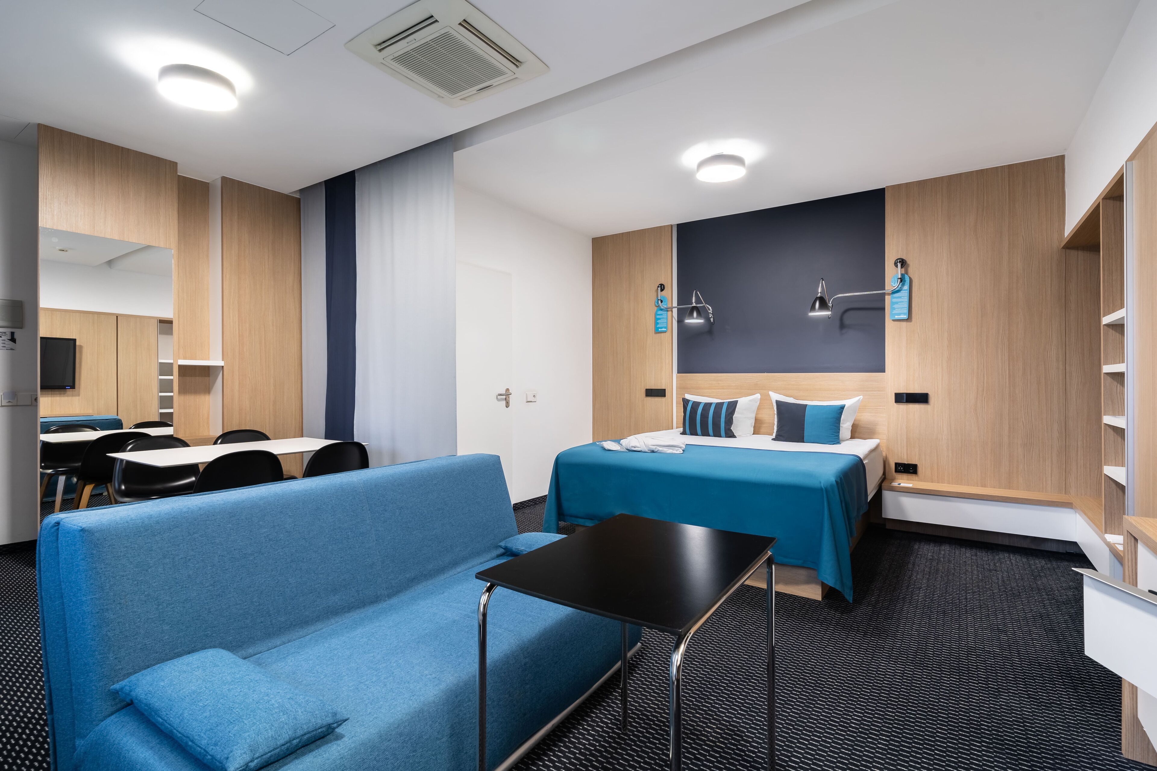 A hotel room with a bed, a sofa, a desk, and a small table.