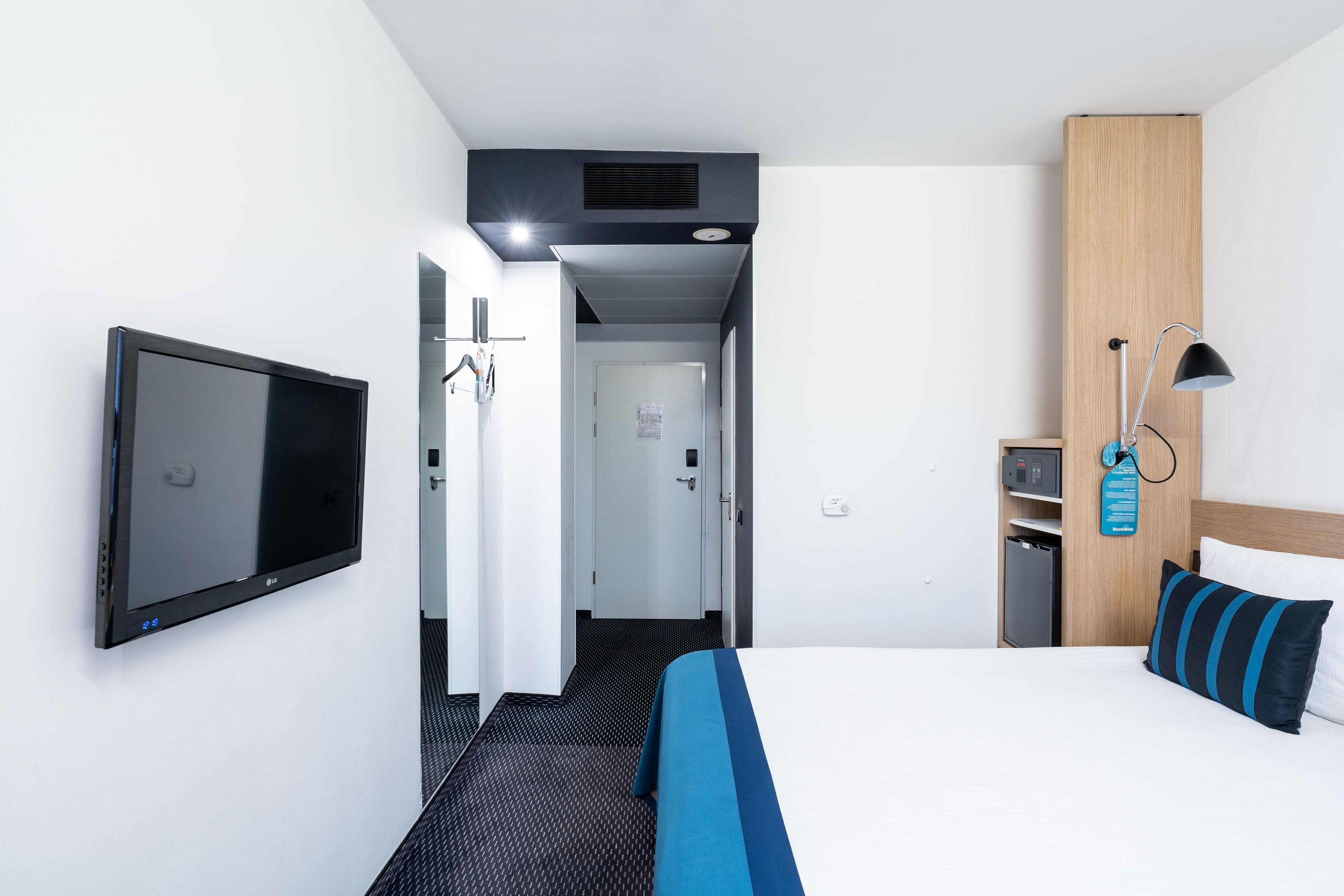 A hotel room with a bed, a television, a desk with a lamp, and a wardrobe.