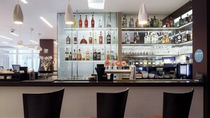 A bar area with shelves of liquor bottles, glasses, and a counter with a coffee machine. There are two chairs in front of the bar. - Bonhotel (Minsk)