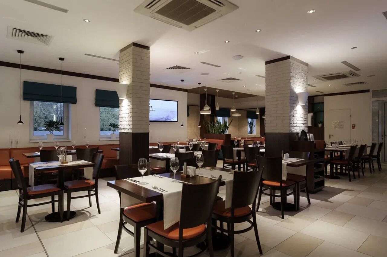 A modern restaurant with high tables and booths, large windows with blinds, and a flat-screen TV on the wall.