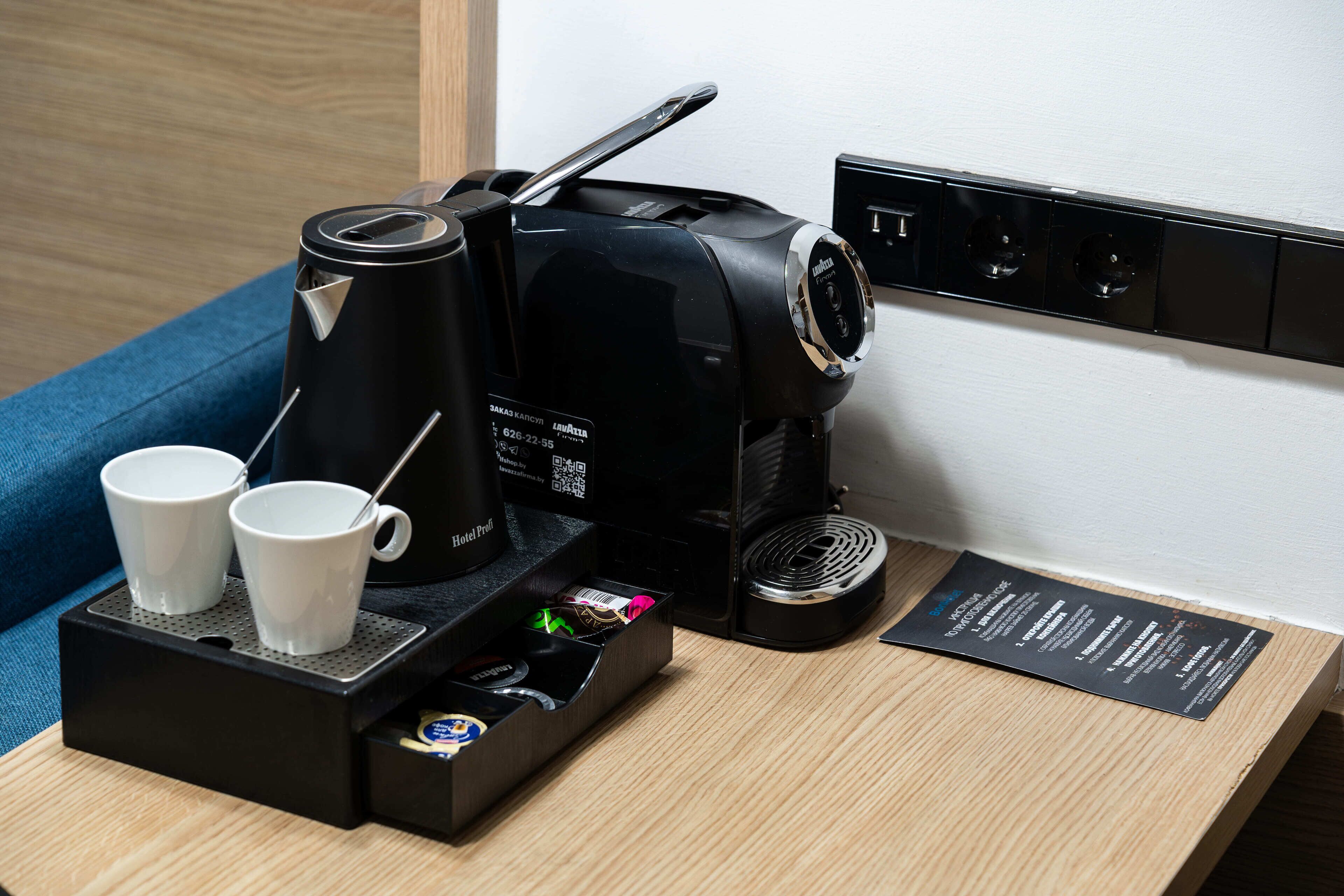 A coffee maker with two cups on a tray, a power outlet, and a menu on the wall.