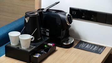 A coffee maker with two cups on a tray, a power outlet, and a menu on the wall.