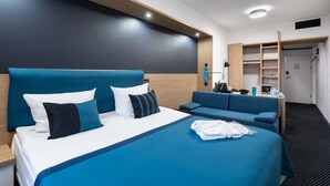 A modern hotel room with a large bed, a sofa, a wardrobe, and a desk with a lamp. - Bonhotel (Minsk)