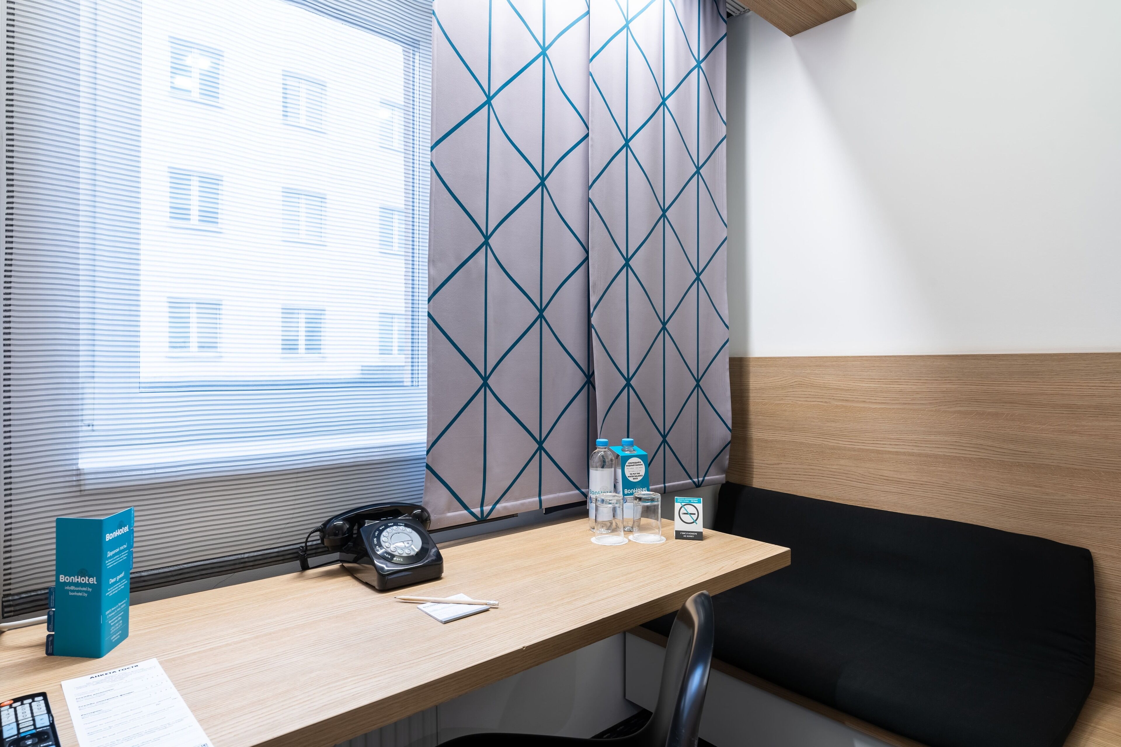 Habitación de hotel con un escritorio de madera, un teléfono negro, una botella de agua, un vaso y un folleto de BonHotel.