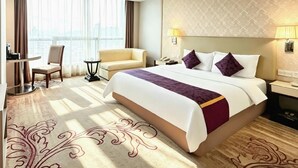 Hotellihuone, jossa on suuri sänky, työpöytä, tuoli ja ikkunasta avautuva näkymä kaupunkiin.
