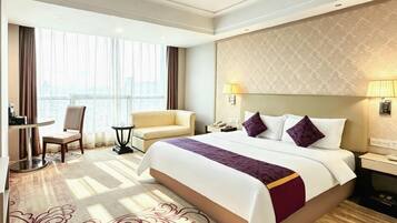 A hotel room with a large bed, a desk, a chair, and a view of the city through the window.