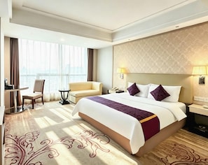 A hotel room with a large bed, a desk, a chair, and a view of the city through the window. - Zongheng Hotel (Qiandongnan)