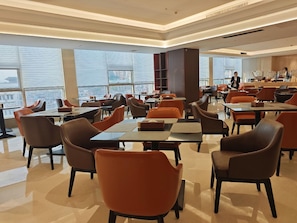 A modern dining area with tables and chairs, large windows, and a view of the city. - Zongheng Hotel (Qiandongnan)