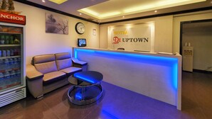 A hotel reception area with a modern design, including a reception desk, a clock, and a seating area with a sofa and a small table. - De UPTOWN Hotel @ Damansara Uptown (Petaling Jaya)