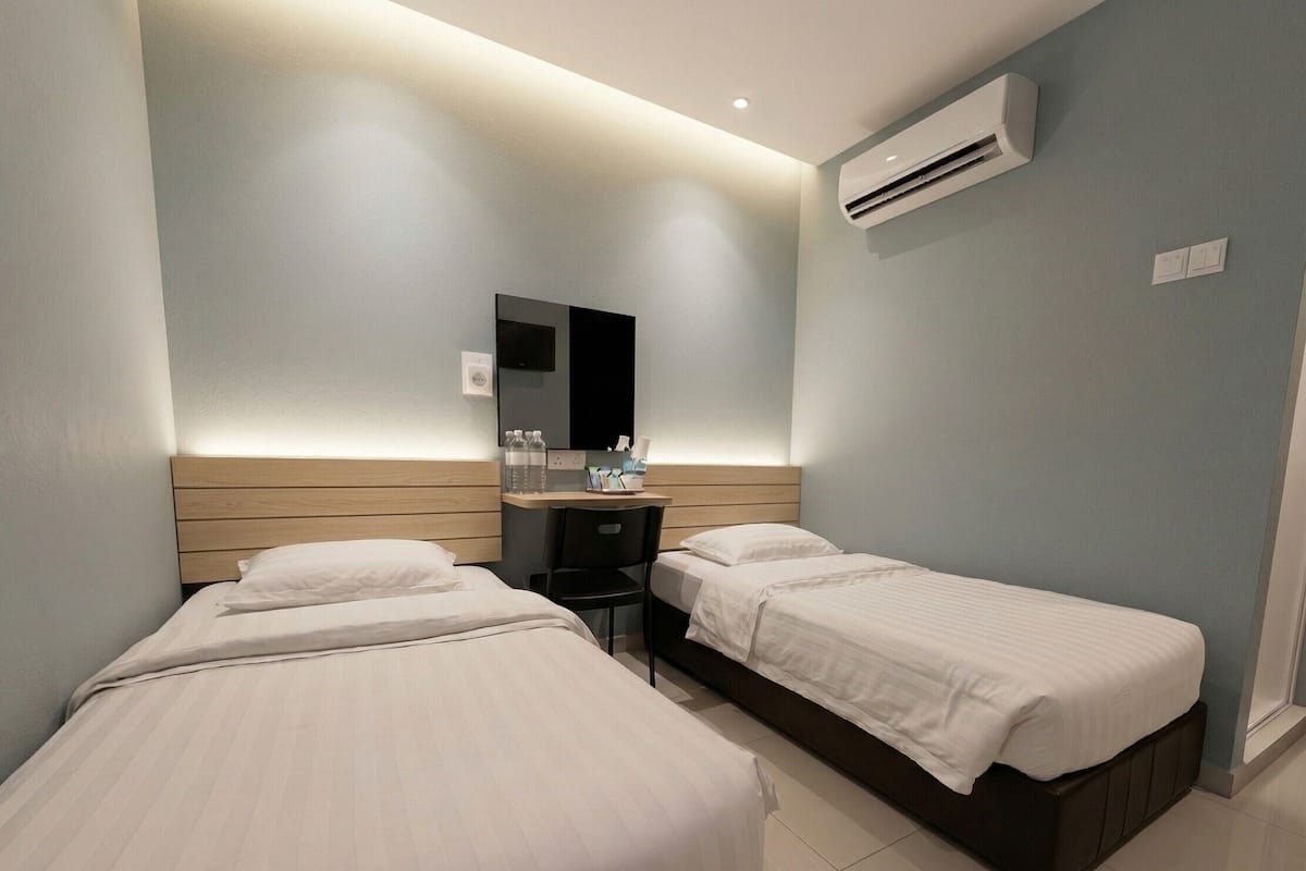 A hotel room with two beds, a desk, a chair, an air conditioning unit, and a mirror.