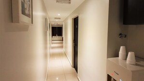 A hotel hallway with a modern design, featuring a long corridor, a mounted television, and a built-in sink with cups. - De UPTOWN Hotel @ Damansara Uptown (Petaling Jaya)