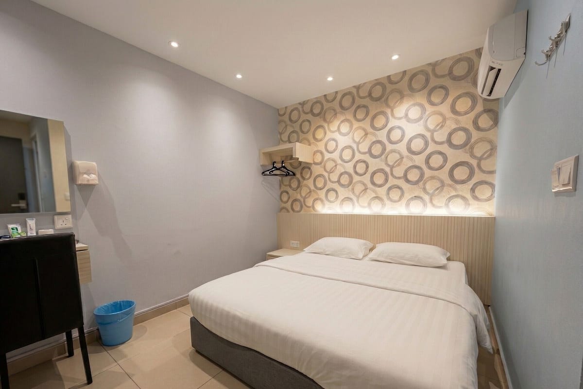 A modern bedroom with a bed, bedside tables, a mirror, and a wall-mounted air conditioning unit.