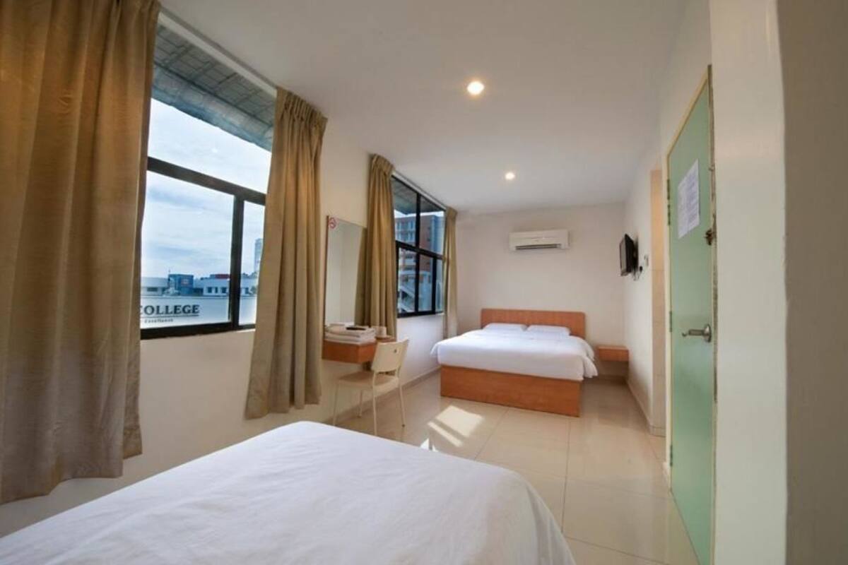Ein Hotelzimmer mit zwei Betten, einem Schreibtisch, einem Stuhl und einem Fenster mit Blick auf ein Gebäude.