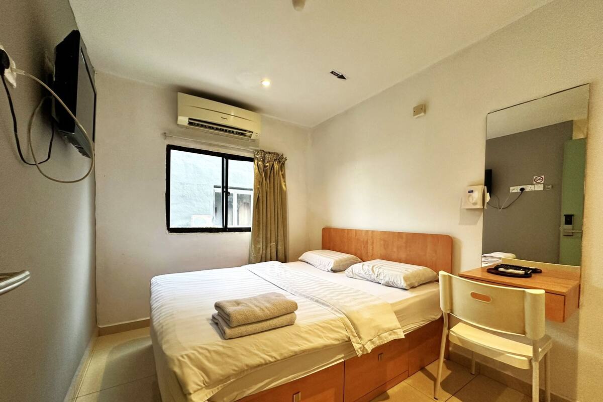 Ein Hotelzimmer mit Bett, Schreibtisch, Stuhl, Klimaanlage, einem Fenster mit Vorhängen und einem Spiegel.
