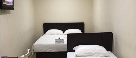 A hotel room with two beds, a desk, a chair, and a television.