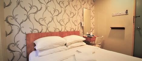 A neatly made bed with white linens and pillows, a wooden headboard, a bedside table with a lamp, and a wall with a patterned wallpaper.