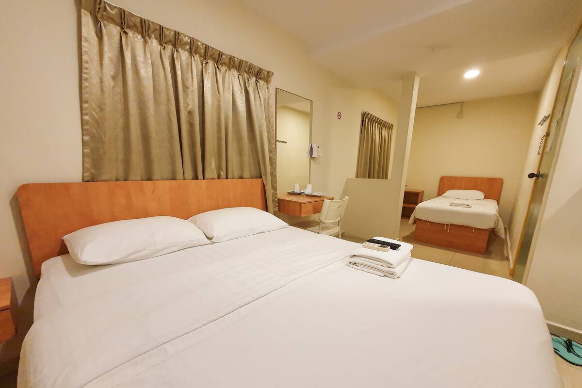 Ein Hotelzimmer mit einem großen Bett, einem Schreibtisch mit Stuhl, einem weiteren Bett und einem durchgegangenen Tür erkennbaren Badezimmer.