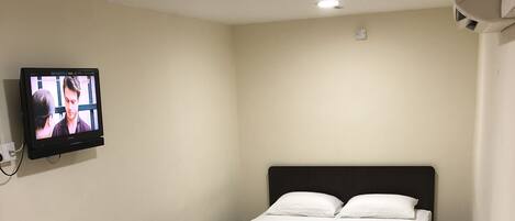 A hotel room with two beds, a TV mounted on the wall, a desk with a chair, and a window with curtains.