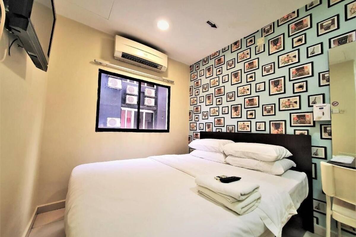 Ein Hotelzimmer mit Bett, Fenster, Klimaanlage, einer Wand mit gerahmten Bildern und einem Schreibtisch mit Stuhl.