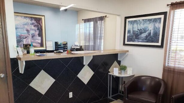 A reception area with a black and white tiled wall, a reception desk, a framed painting, a chair, and a window with curtains. - Executive Inn Woodward (Woodward)