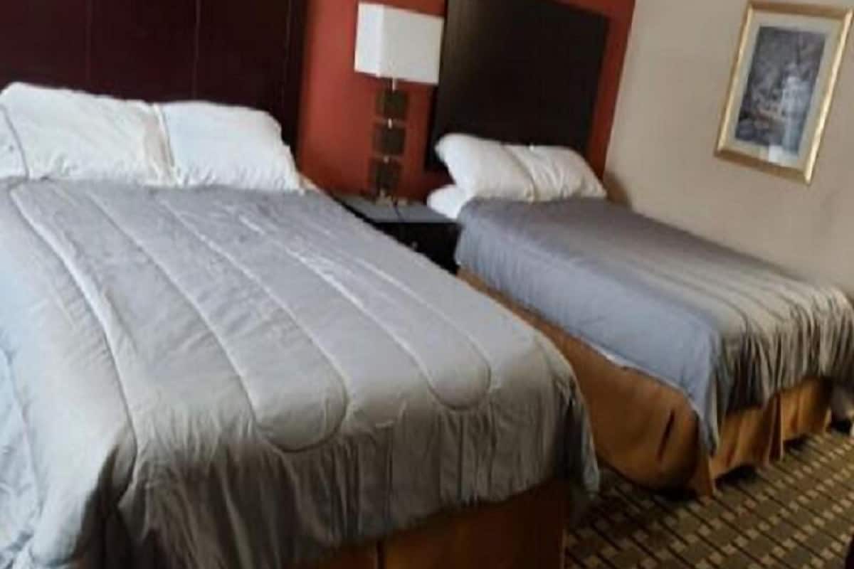 A hotel room with two single beds, a nightstand with a lamp, and a framed picture on the wall.