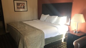 A hotel room with a bed, a nightstand with a lamp, a framed picture on the wall, and a patterned carpet. - Executive Inn Woodward (Woodward)