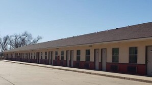 A row of single-story motel rooms with individual doorways and windows, a flat roof, and a concrete parking lot. - Executive Inn Woodward (Woodward)