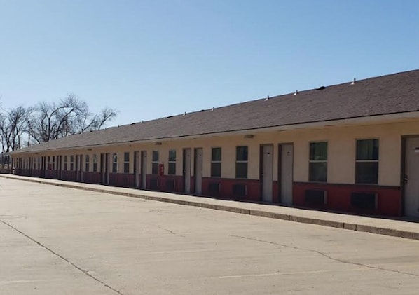 Fileira de quartos de motel térreos, cada um com porta e janela individual, teto plano e estacionamento de concreto.