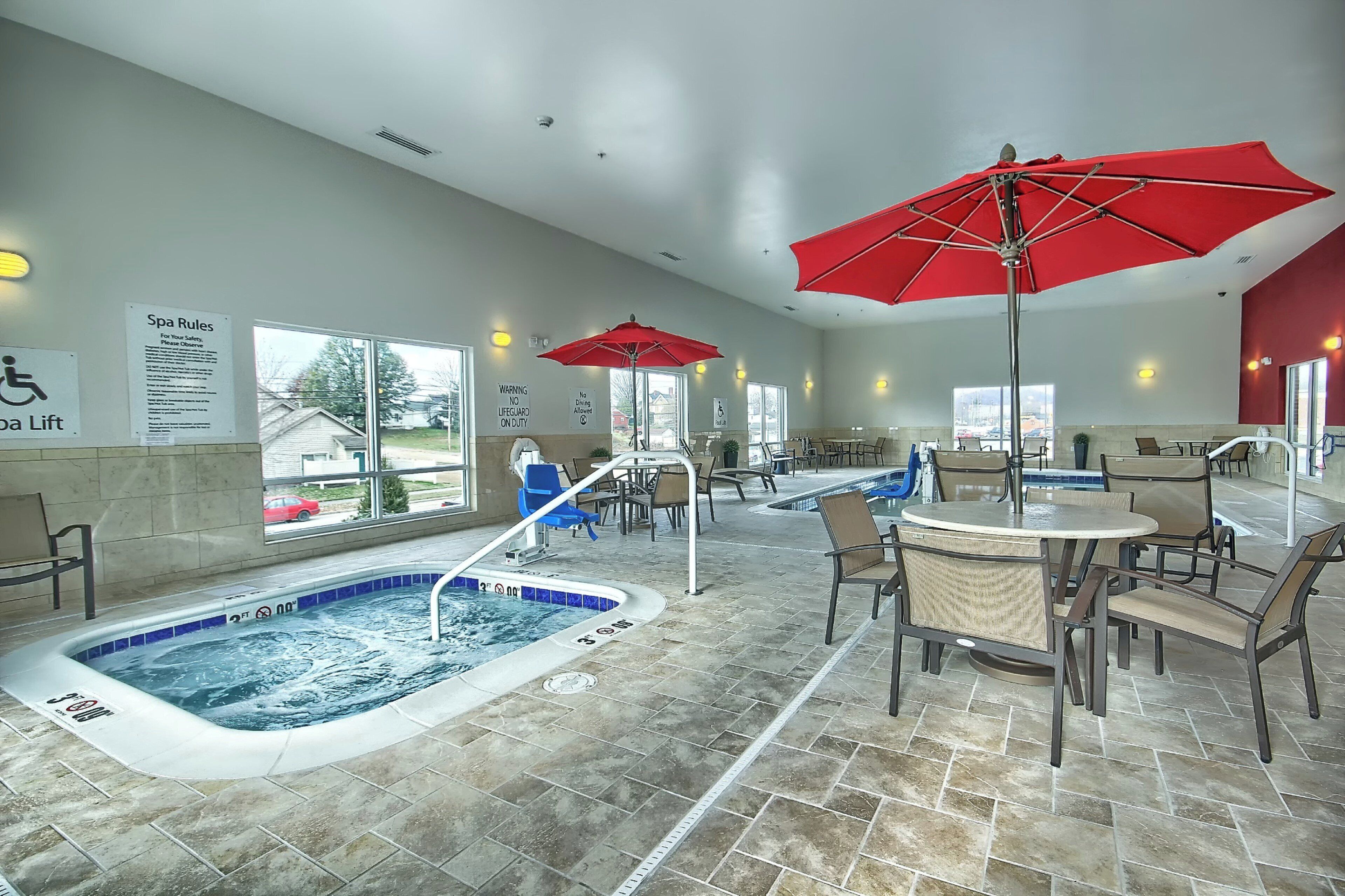 Un área de spa con un jacuzzi, asientos y sombrillas rojas.