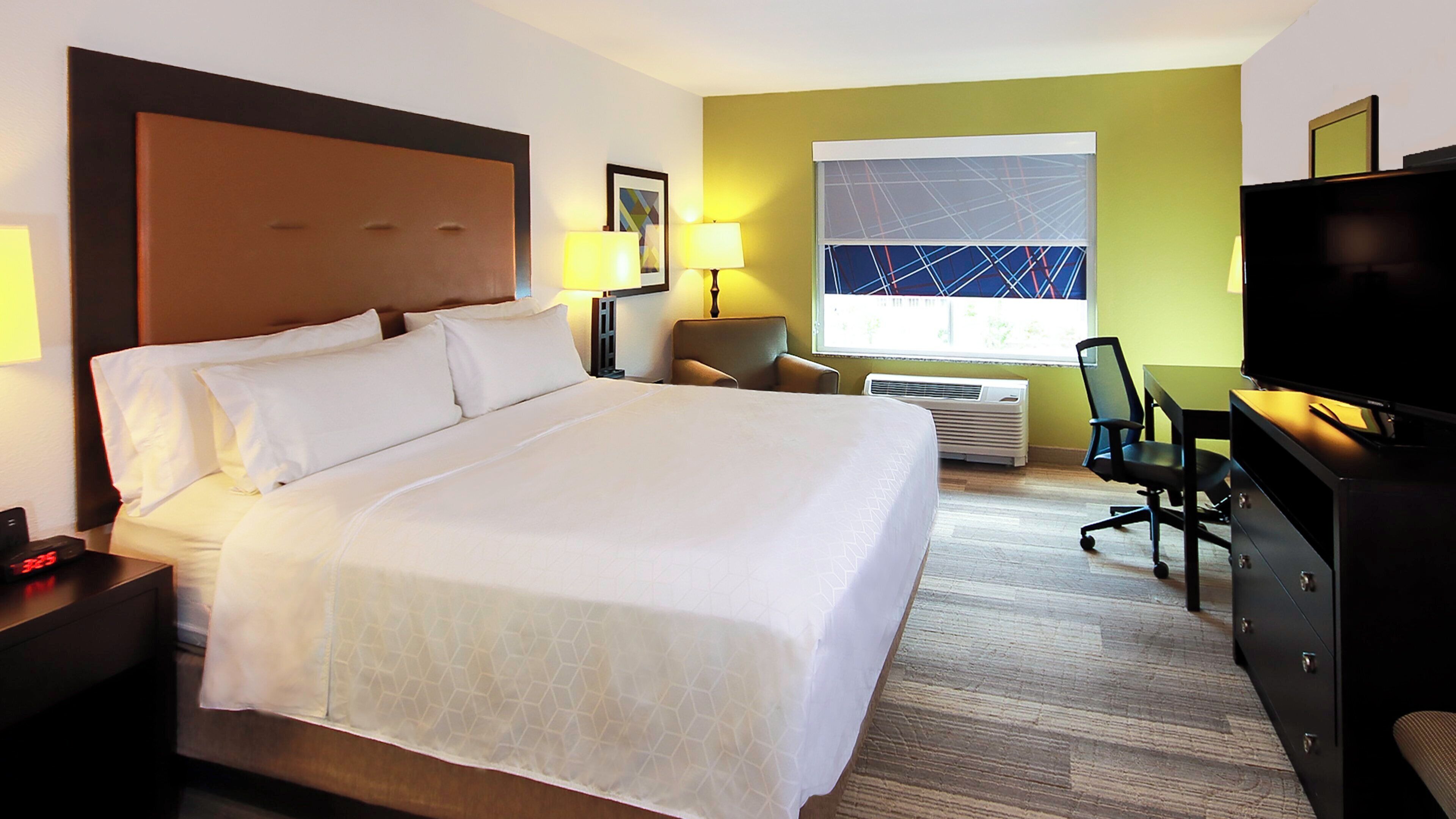 Habitación de hotel con una cama grande, un escritorio con silla, televisión y ventana con vistas.