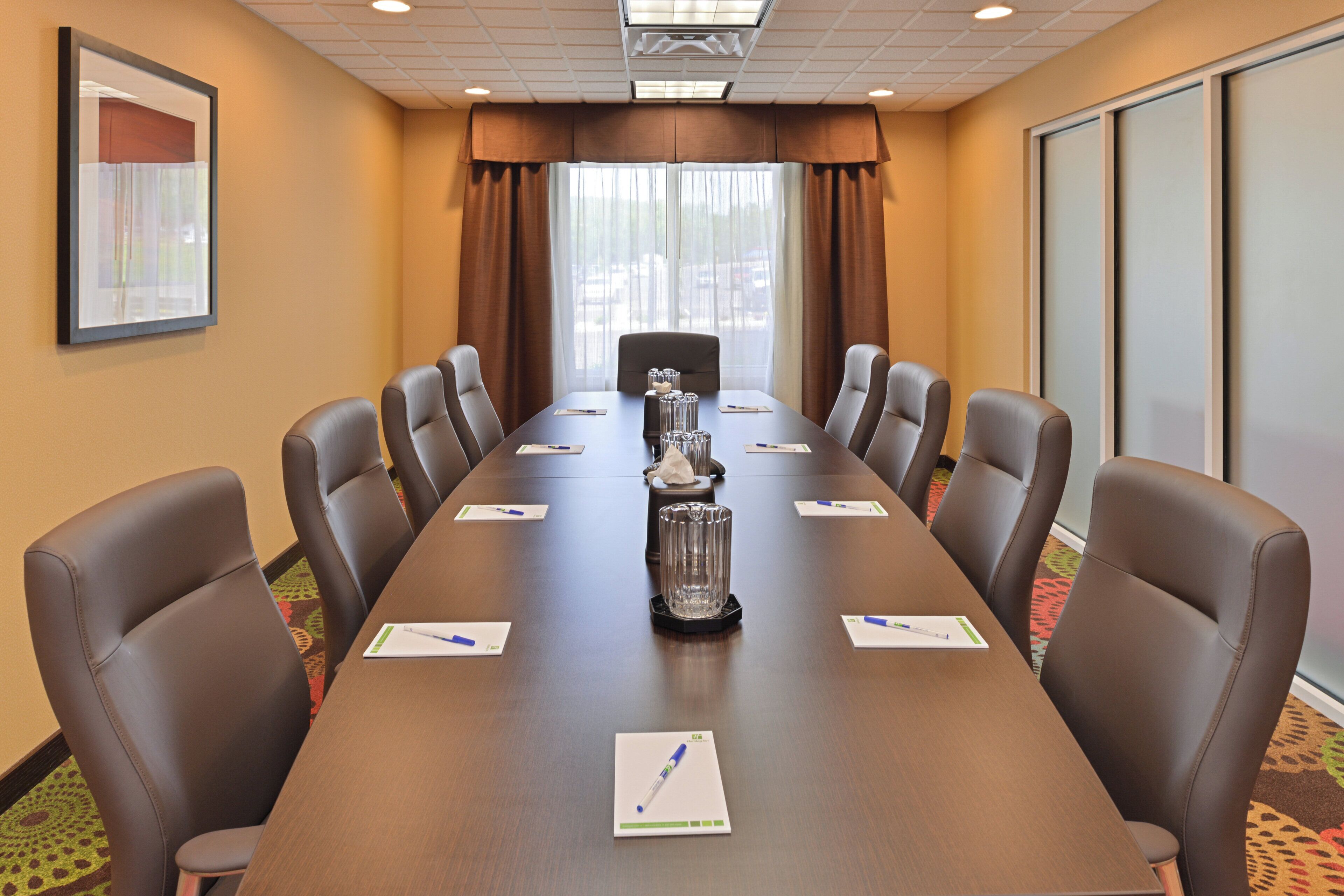 A conference room with a long table, chairs, a projector screen, and a window with curtains.