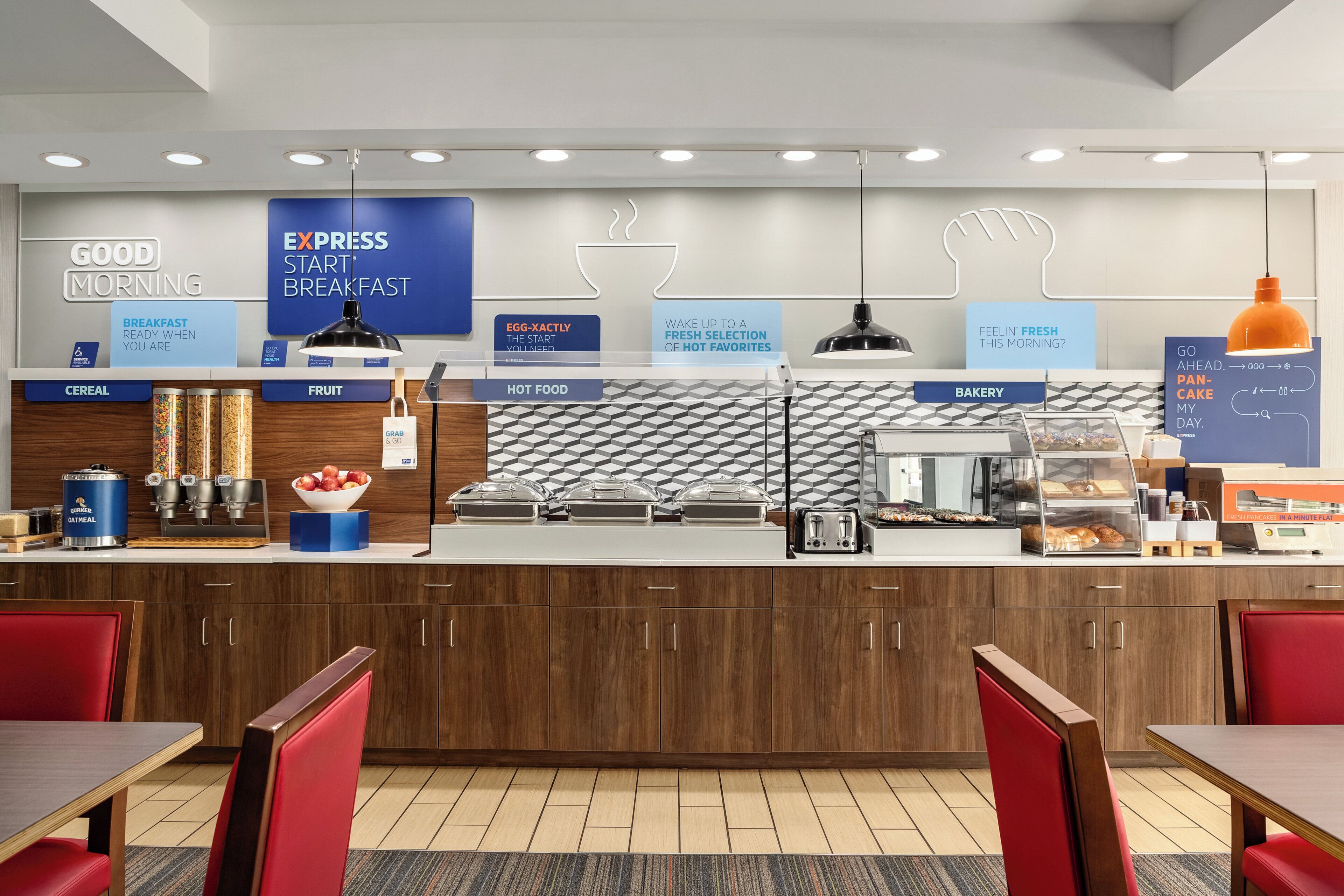 A breakfast area with labeled sections for cereal, fruit, hot food, and bakery, and a counter with various breakfast items.