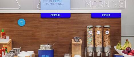 A breakfast bar with labeled sections for cereal and fruit, a kettle, and condiments.
