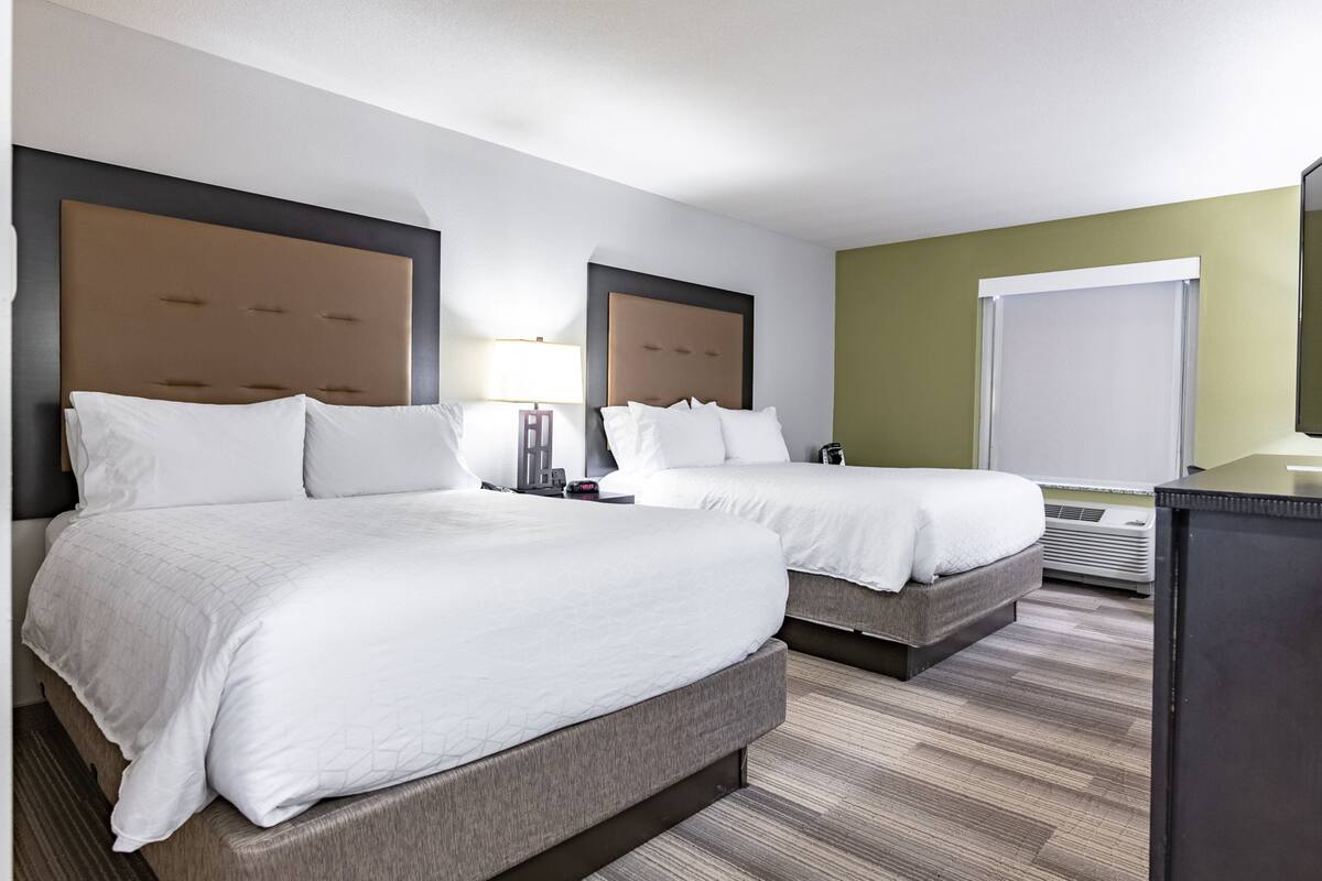 A hotel room with two beds, a desk, a chair, a lamp, and a window.
