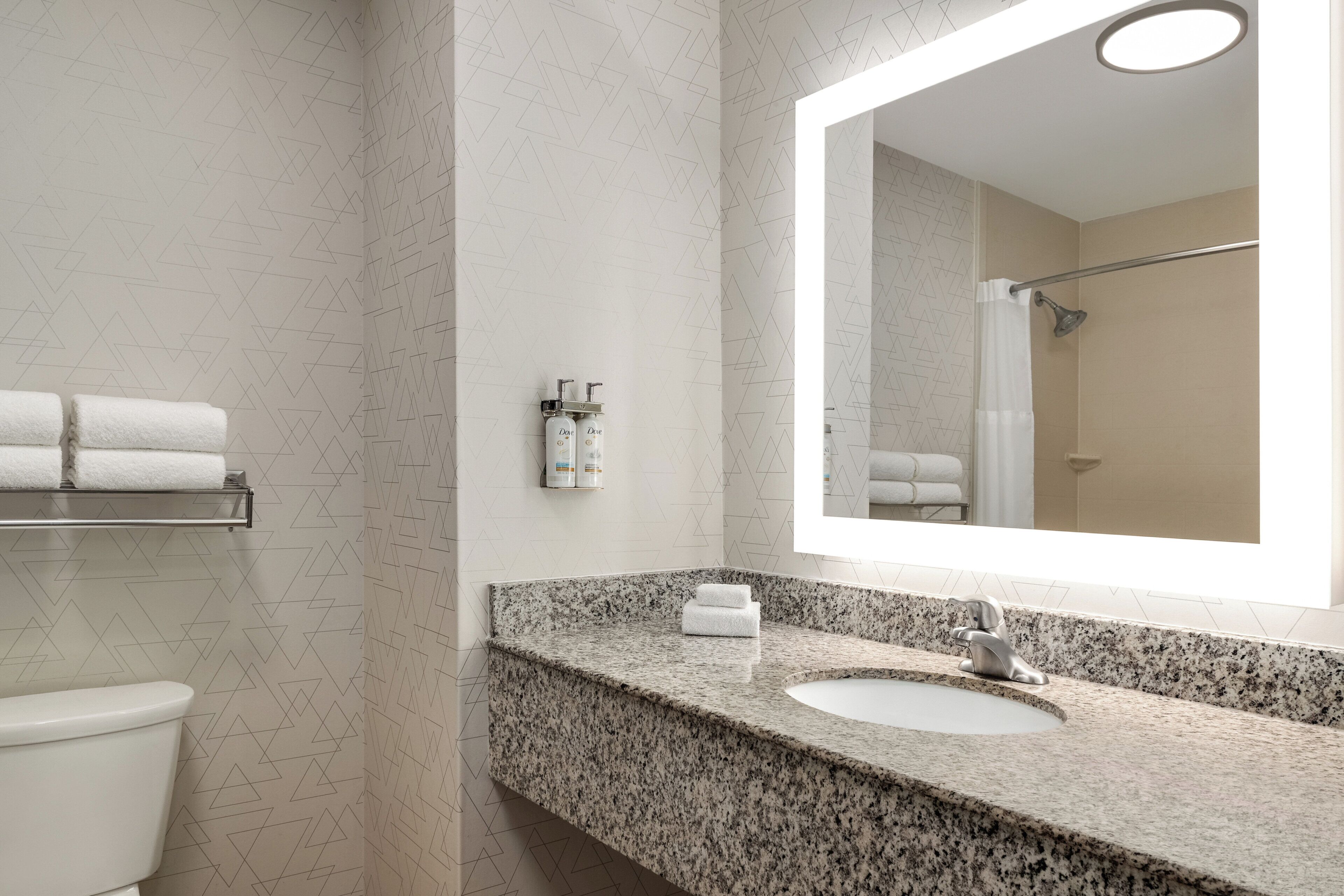 A bathroom with a granite countertop, a sink, a mirror, and a shower.