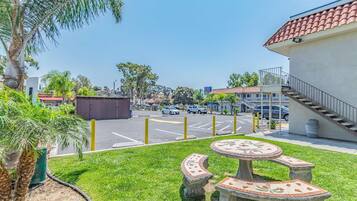 A parking lot with a building in the background, a grassy area with a decorative stone table, and a palm tree.