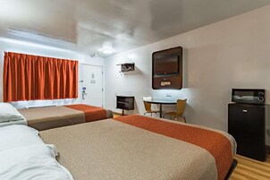 Habitación de hotel con dos camas, un escritorio, una silla, un refrigerador pequeño y una televisión.