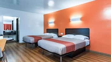 A hotel room with two beds, a wooden floor, and a red accent wall.
