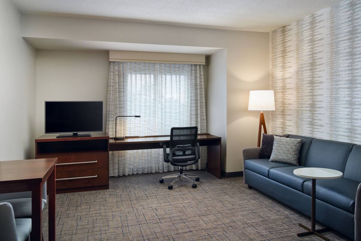 Une chambre d’hôtel équipée d’un bureau, d’une télévision, d’un canapé, d’une petite table et d’une lampe.