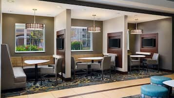 A hotel lobby with seating areas, tables, and a large window offering a view of greenery.