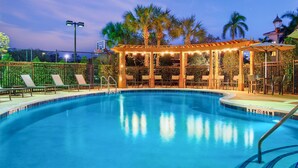 A swimming pool with lounge chairs and a covered seating area with string lights.