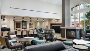 A hotel lobby with a seating area featuring sofas, chairs, and tables, a fireplace, and a large window offering a view of the outside.