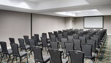 Uma sala de conferências com fileiras de cadeiras, uma tela grande e um tapete estampado.