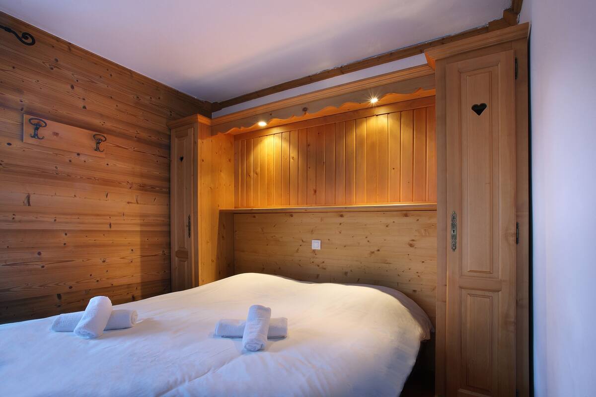 Une pièce aux murs lambrissés, avec un lit, deux serviettes sur le lit et une porte ornée d’une découpe en forme de cœur.