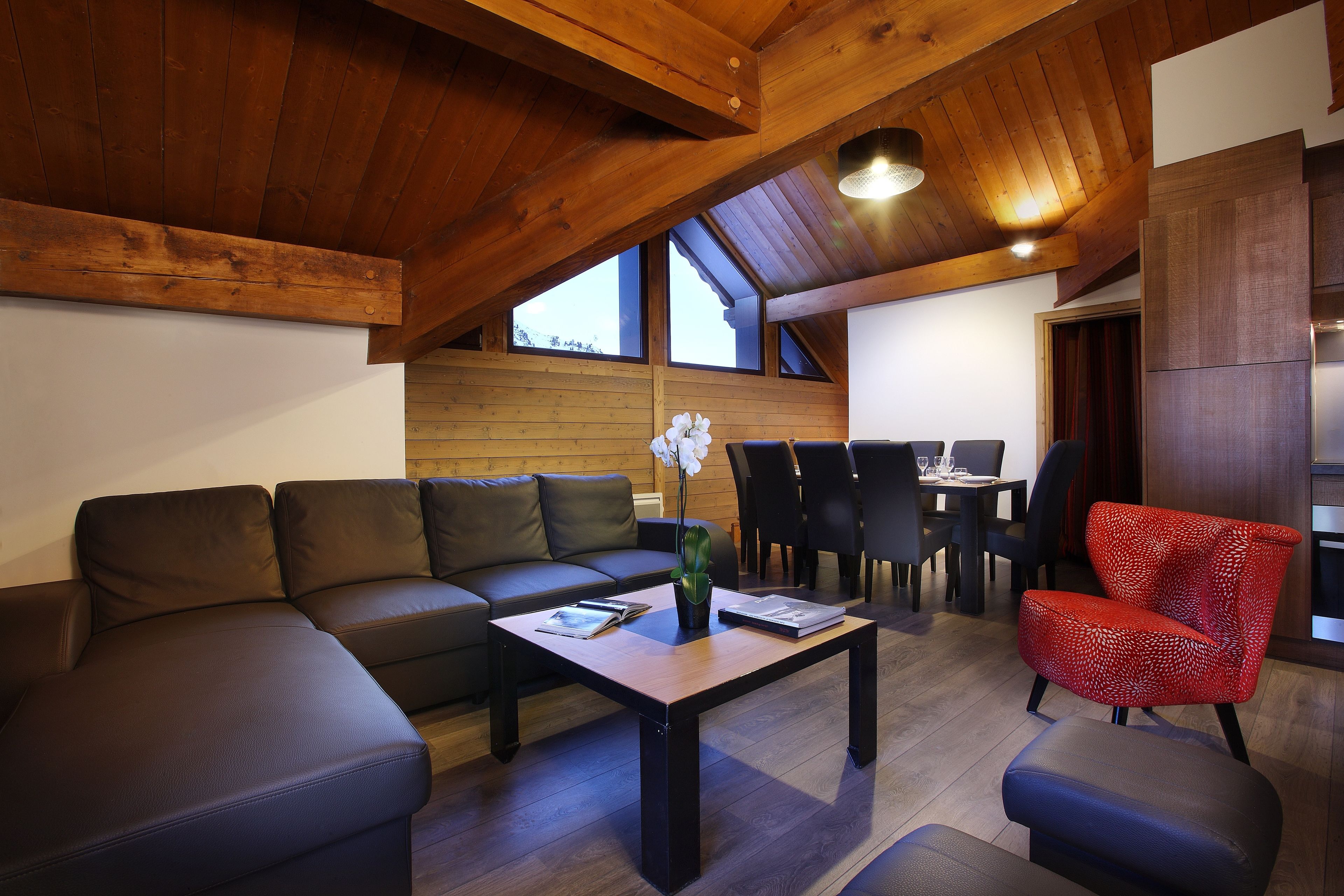 Een moderne woonkamer met een hoekbank, een salontafel, een rode fauteuil en een eethoek met een tafel en stoelen.