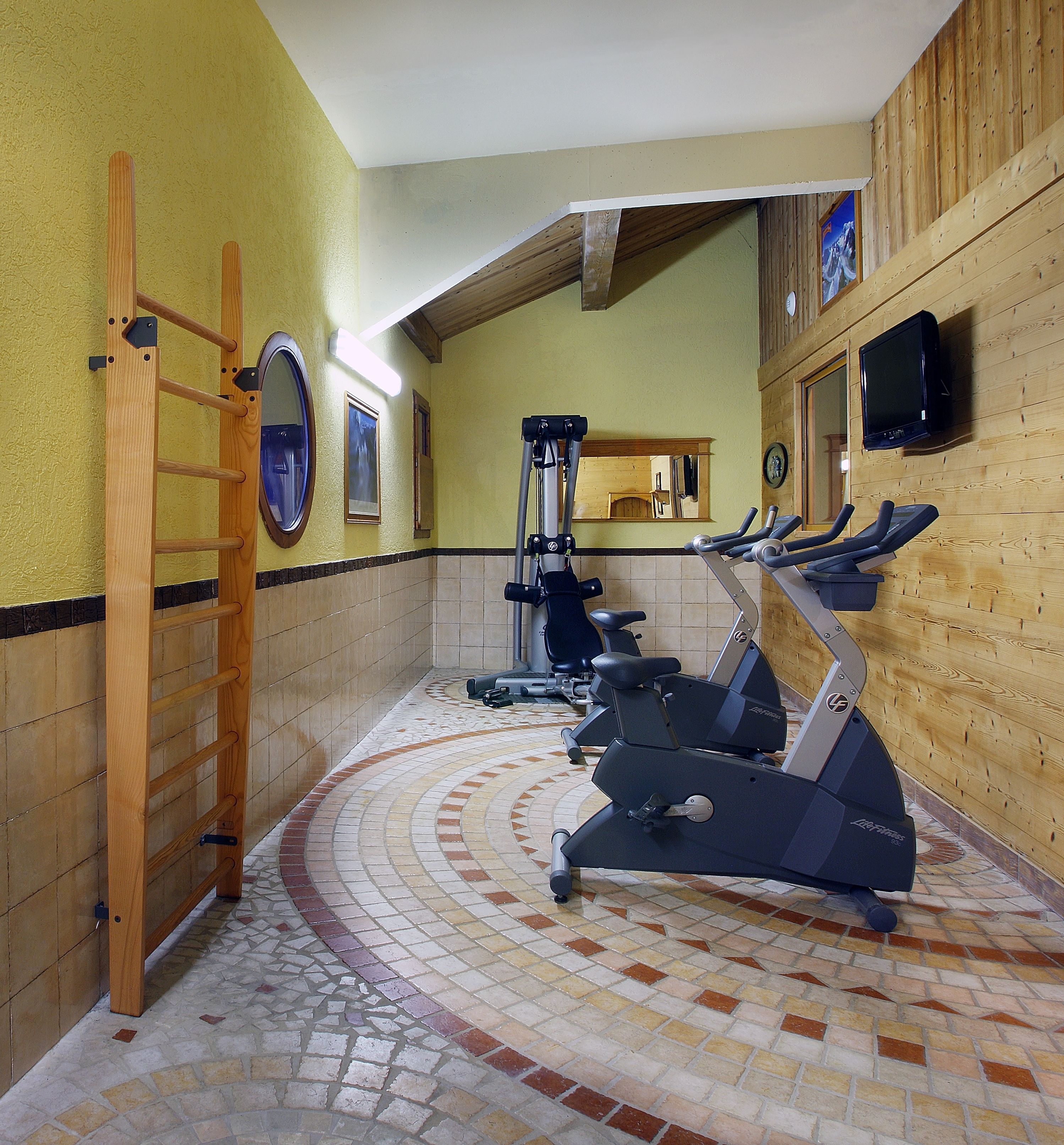 Un gimnasio con equipamiento de ejercicio, una escalera de madera y piso de baldosas.