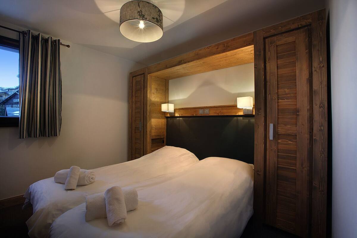 Une chambre à coucher comprenant un lit, une tête de lit avec un miroir, deux lampes de chevet et une fenêtre avec des rideaux.