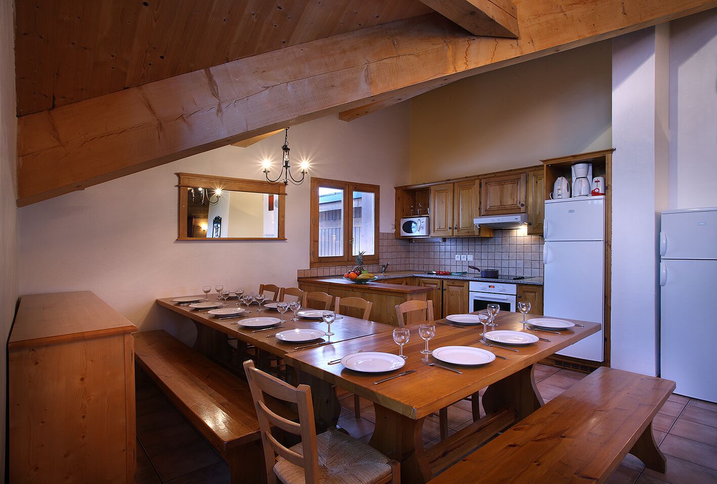 Un coin repas avec une table en bois dressée pour quatre personnes, des chaises en bois, un banc en bois et un plafond en bois.